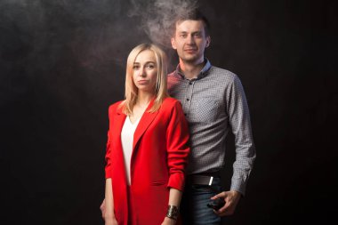 Genç güzel beyaz ceket ve beyaz bluz ve uzun boylu esmer adam duman ve izole siyah arka plan karşı sarılma ile parlak kırmızı elbiseli sarışın kız