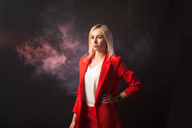 Genç beyaz sarışın kız güzel bir ceket ve beyaz bluz ile sıkı takım elbise kameraya bir arka plan üzerinde görünüyor parlak kırmızı mavi renkli ve arka plan üzerinde siyah pembe duman izole