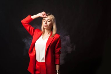 Genç beyaz sarışın kız güzel bir ceket ve beyaz bluz ile sıkı takım elbise kameraya bir arka plan üzerinde görünüyor parlak kırmızı mavi renkli ve arka plan üzerinde siyah pembe duman izole