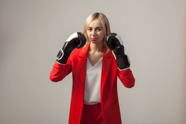 Bir ceket ve beyaz bluz ayakta beyaz izole arka planda boks eldivenli bir poz ile kırmızı sıkı elbiseli Genç güzel beyaz sarışın kız