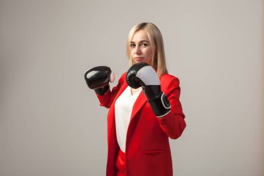 Bir ceket ve beyaz bluz ayakta beyaz izole arka planda boks eldivenli bir poz ile kırmızı sıkı elbiseli Genç güzel beyaz sarışın kız