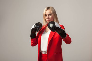 Bir ceket ve beyaz bluz ayakta beyaz izole arka planda boks eldivenli bir poz ile kırmızı sıkı elbiseli Genç güzel beyaz sarışın kız