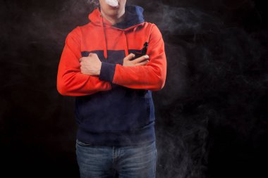 Genç esmer biri yakın duruş içinde renkli bir turuncu ve mavi kapüşonlu daimi bir vape içiyor ve bir beyaz siyah bir izole arka plan üzerinde duman exhales