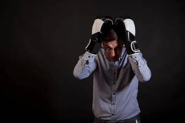 Dark-haired man in a plaid shirt with boxing gloves on his hands clings to the head  thinking about the problem on black isolated background