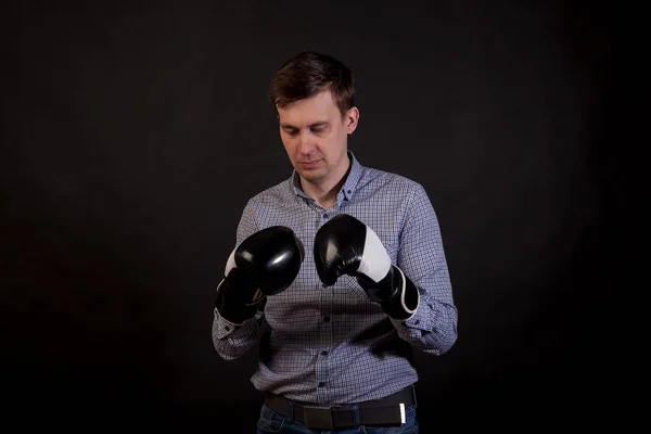Dark-haired man in a plaid shirt with boxing gloves on his hands in stance on black isolated background