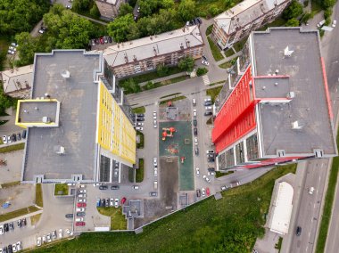 Kırmızı ve sarı renk ile otomobil ve yeşil ağaçlar ve çalılar ile bahçede çocuk oyun Park yeri küçük binalar arasında iki uzun boylu gökdelenlerin hava üstten görünüm
