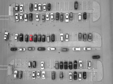 Aerial view of a large number of black-and-white and gray cars parked in a parking lot near a shopping center in a chaotic manner among several red cars separated by white stripes clipart