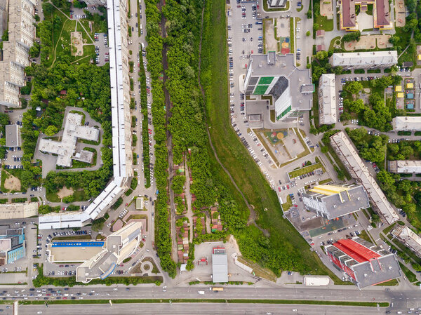 Aerial top view of two tall skyscrapers of red and yellow colors among small buildings with parking for cars and a children's playground in the yard with green trees and shrubs