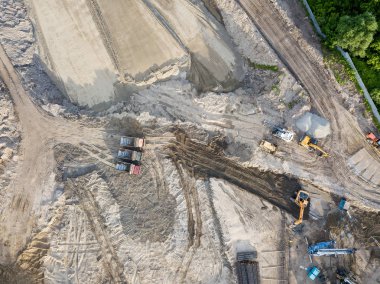 İnşaat alanında bir sondaj teçhizat, ekskavatör ve üç kamyon toprak ulaşım için yüklenmesini beklemek ile zemin hazırlanması ve inşaat ilk aşamada üstten görünüm