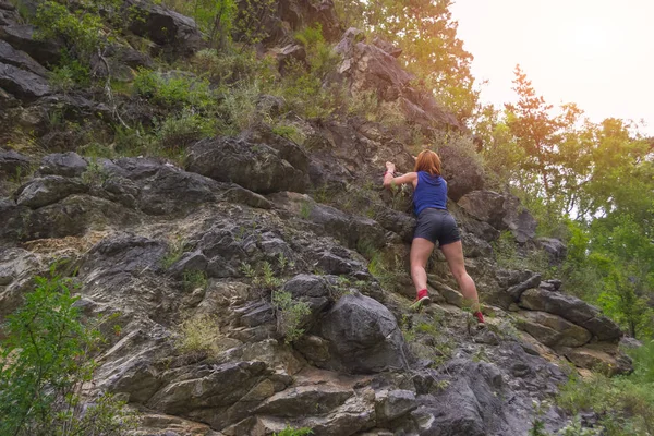 Young red-haired women climber in sports clothes climbs on rocks to the top in mountains of Altai without equipment and insurance