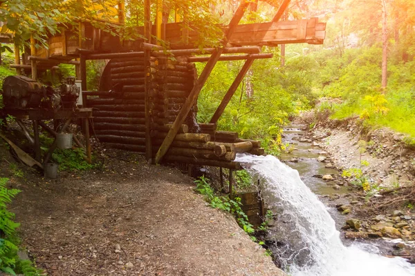 An old water mill in the mountains of the Altai producing electricity, through which water flows forming a waterfall spraying drops with shining sun