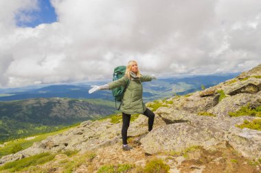 sarışın turist altay gülümsüyor, dağlarda bir sırt çantası konumu olan gözlerinin arkasında dağ zirveleri güneşe kollarını zevk kapanır ile uzanır. Kızı dağa tırmanıyor.