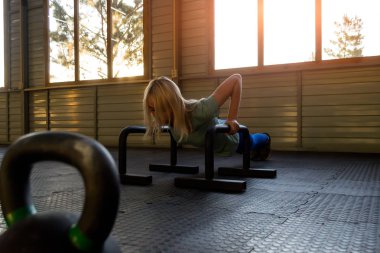 sarışın kız olduğunu yüzü ve ağaçlar ve güneş ışınları görebilirsiniz büyük pencereler ile spor salonunda aşağı gövde düşürücü push-up yüklü crossbeams gelen lastik minderin üzerine monte