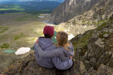 sevgi dolu bir çift bir kaya kenarında oturan onları önünde bir ısmarlayarak dağlar, kar ile turkuaz göller Vadisi ve mavi gökyüzü beyaz bulutlar ile kucaklayan. Arkadan görünüş beni izleyin