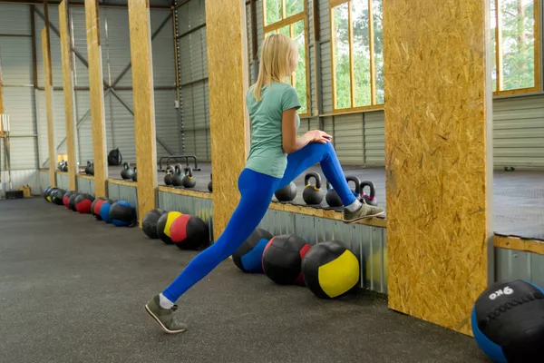 Spor malzemeleri ve simülatörleri arka plan üzerinde spor salonunda onun diz elleriyle bir bankta kadar onun bacak Germe mavi tozluk sarışın kız yok, belgili tanımlık pencere eşiği-ebilmek var olmak seen içinde ağaçlar.