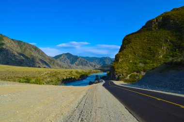 Bir yeni asfalt siyah yol şerit kayalar ve bulutlar ve sonbahar çimleri ile kaplı bir alan ile açık mavi gökyüzü altında altay dağlarında Katun Nehri arasında bölen bir sarı ile