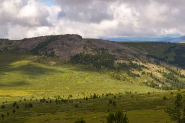 Yeşil vadi peyzaj yemyeşil yeşil çimen, ışıkla ile dağlar, kaplı taş ve hills, mavi gökyüzü beyaz bulutlar ve Altay Dağları'nda güneş ışınları altında bir taze yaz günü ile sular altında