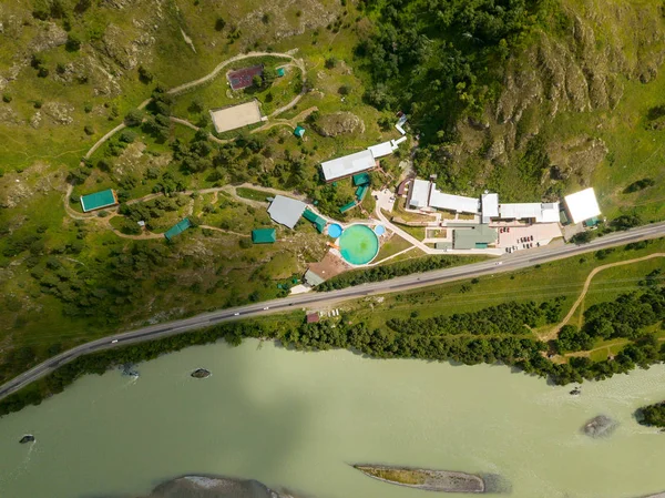 A sports and tourist base with swimming pools and recreational and sports facilities located near the road and the Katun River in the mountains of the Altai on a bright sunny day on the slope of the mountain