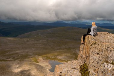 Sarışın kız tehlikeli yalnız yukarıda bacaklarını aşağı göl üzerinde asılı ve tepeler tepeler üzerinde bulutları içine bakan altay dağlarında uçurum uçurum kenarına oturur.