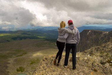 Sevgi dolu bir çift arka plan banyo güneş ışığı, tepeler, buzullar, kayalar kar ve beyaz bulutlar ile mavi göller bir vadinin sarılma dağda duruyor.