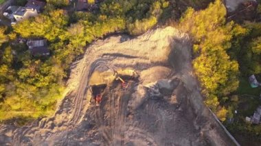 Bir taş ocağında, biri eski evleri ve yeşil sarı ağaçlar ortasında bir şantiye yakınlarındaki bir tepe dibinde toprak sonbaharda ayıklar duran iki portakal Ekskavatör havadan görünümü