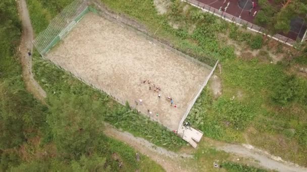 Vue aérienne d'une aire de jeux de football sportive en sable située dans les montagnes de l'Altaï au sommet d'une falaise avec une équipe de joueurs lors d'une séance d'entraînement en plein air lors d'une chaude journée d'été parmi les arbres verts 