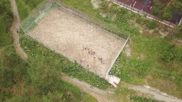 緑の木々 の中で暖かい夏の日に屋外の試しの間にプレーヤーのチームが崖の上にアルタイ山脈にある砂で作られたスポーツ サッカー遊び場の空中写真 — ストック動画