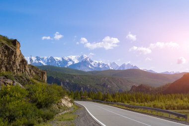 Cliff üzerinde en fazla mavi gökyüzü ve bulutlar, altay güvenlik günbatımında bir çit road yakınındaki beyaz buzullar yüksek karla kaplı dağlarla zemin karşı yakınındaki asfalt yol virajlı