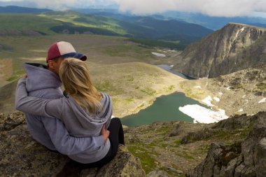 sevgi dolu bir çift bir kaya kenarında oturan onları önünde bir ısmarlayarak dağlar, kar ile turkuaz göller Vadisi ve mavi gökyüzü beyaz bulutlar ile kucaklayan. Arkadan görünüş beni izleyin