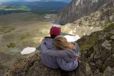 sevgi dolu bir çift bir kaya kenarında oturan onları önünde bir ısmarlayarak dağlar, kar ile turkuaz göller Vadisi ve mavi gökyüzü beyaz bulutlar ile kucaklayan. Arkadan görünüş beni izleyin
