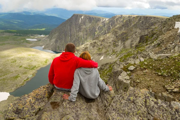 sevgi dolu bir çift bir kaya kenarında oturan onları önünde bir ısmarlayarak dağlar, kar ile turkuaz göller Vadisi ve mavi gökyüzü beyaz bulutlar ile kucaklayan. Arkadan görünüş beni izleyin