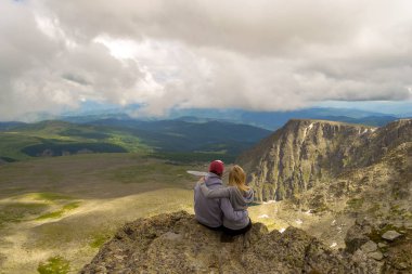 sevgi dolu bir çift bir kaya kenarında oturan onları önünde bir ısmarlayarak dağlar, kar ile turkuaz göller Vadisi ve mavi gökyüzü beyaz bulutlar ile kucaklayan. Arkadan görünüş beni izleyin