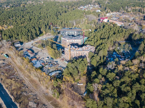 Aerial view of the construction of three elite residential buildings on the river bank in the middle of a green coniferous forest with a favorable environment, a lot of equipment costs near the site