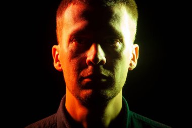 Anız, karanlıkta, bir gömlek giymiş olan bir adam bir tıraşsız yüzü yüzü Close-up sarı bir tarafta aydınlatılmış ve diğer kırmızı bir siyah arka plan izole