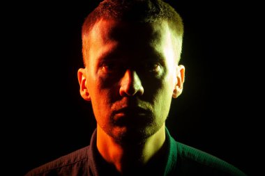 Anız, karanlıkta, bir gömlek giymiş olan bir adam bir tıraşsız yüzü yüzü Close-up sarı bir tarafta aydınlatılmış ve diğer kırmızı bir siyah arka plan izole