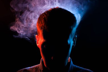 Adamın yüzünü siyah Yalıtılmış zemin kırmızı ve mavi vape duman ile gölgelerde gizli. Yabancı düşünceler.