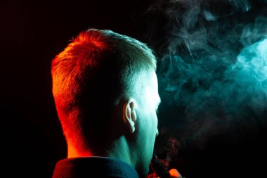 Bir vape sigara ve çok renkli duman yeşil ve kırmızı farklı yönden kendini izole bir siyah arka plan üzerine adlı parçasıyla birlikte kullanılmalıdır gömlekli bir adam kafasına arkadan görünüm