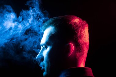 Arkasından bir görünüm bir adamın başının etrafında bir gömlek yasaktır ve siyah Yalıtılmış zemin kendisinden farklı iki taraf için de mavi exhaling çok renkli duman. 