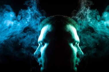 Bir vape sigara ve çok renkli duman yeşil ve mavi siyah Yalıtılmış zemin kendisinden farklı yönlere exhaling gömlekli bir adamın yüzünü ayna görüntüsünü. İnsan ruhu ve düşüncelerini.