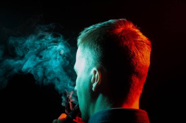 Bir vape sigara ve exhaling gömlekli çocuklar kafasının arkasına bir görünüm çok renkli duman yeşil sol tarafa kendisinden bir siyah arka plan izole. İnsan sağlığına zarar