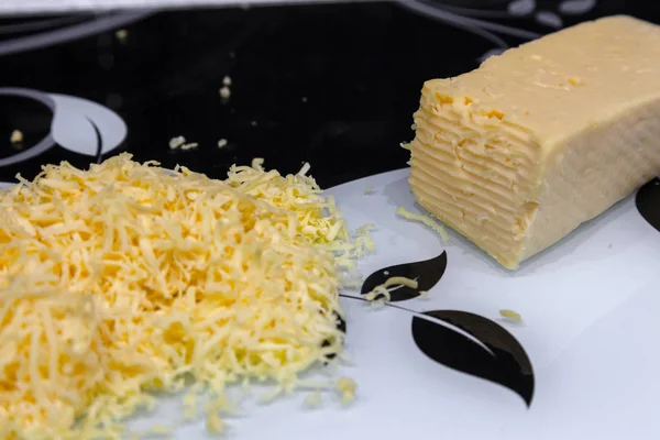 Grated yellow cheese on a glass cutting board in black and white for making breakfast sandwiches using a metal grater