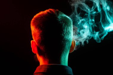Bir vape sigara ve exhaling gömlekli bir çocuğun kafasına arkadan görünüm yeşil dumana doğru yönde kendinden renkli ve arka plan arkadan aydınlatmalı kırmızı üzerine siyah yaptı ile izole