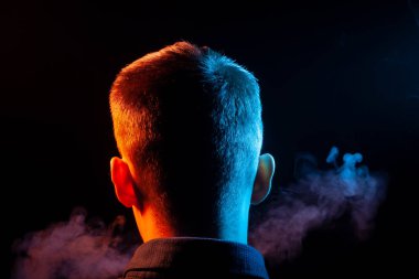 Bir vape sigara ve çok renkli duman mavi ve kırmızı farklı yönden kendini izole bir siyah arka plan üzerine adlı parçasıyla birlikte kullanılmalıdır gömlekli bir çocuğun kafasına arkadan görünüm