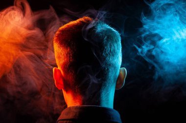 Bir vape sigara ve çok renkli duman mavi ve kırmızı farklı yönden kendini izole bir siyah arka plan üzerine adlı parçasıyla birlikte kullanılmalıdır gömlekli bir çocuğun kafasına arkadan görünüm