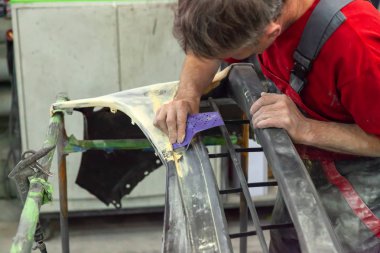 Bir kaza araba zımpara kağıdı yardımıyla onardıktan sonra dükkanı bir adam araba body öğesi boyama için hazırlar. Kurtarma bir çarpışmadan sonra tampon.