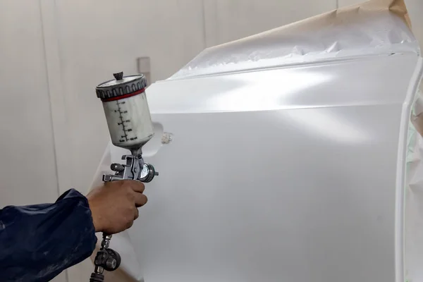 Bir erkek işçi kaza sırasında zarar görmüş sonra beyaz araba vücut parçası boya tabancası ile boyar. Araç onarım atölye sırasında kapıdan.