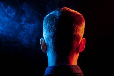 Bir vape sigara ve çok renkli duman mavi ve kırmızı farklı yönden kendini izole bir siyah arka plan üzerine adlı parçasıyla birlikte kullanılmalıdır gömlekli bir adam kafasına arkadan görünüm