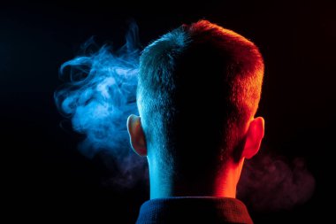 Bir vape sigara ve çok renkli duman mavi ve kırmızı farklı yönden kendini izole bir siyah arka plan üzerine adlı parçasıyla birlikte kullanılmalıdır bir gömlekli bir adam kafasına arkadan görünüm