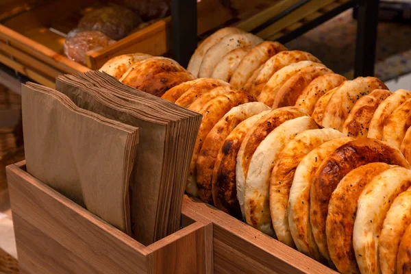 Close-up of tandyr bread cakes freshly baked appetizingly laid out in even rows on the counter of a shopping center in the bakery section with paper packaging bags secured in a wooden stand