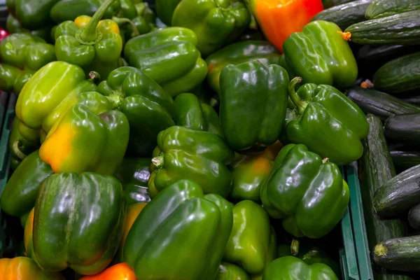 Green, fresh, juicy bell peppers with yellow specks on the sides lie next to other vegetables on the store shelf close up against the background of cucumbers and red peppers.